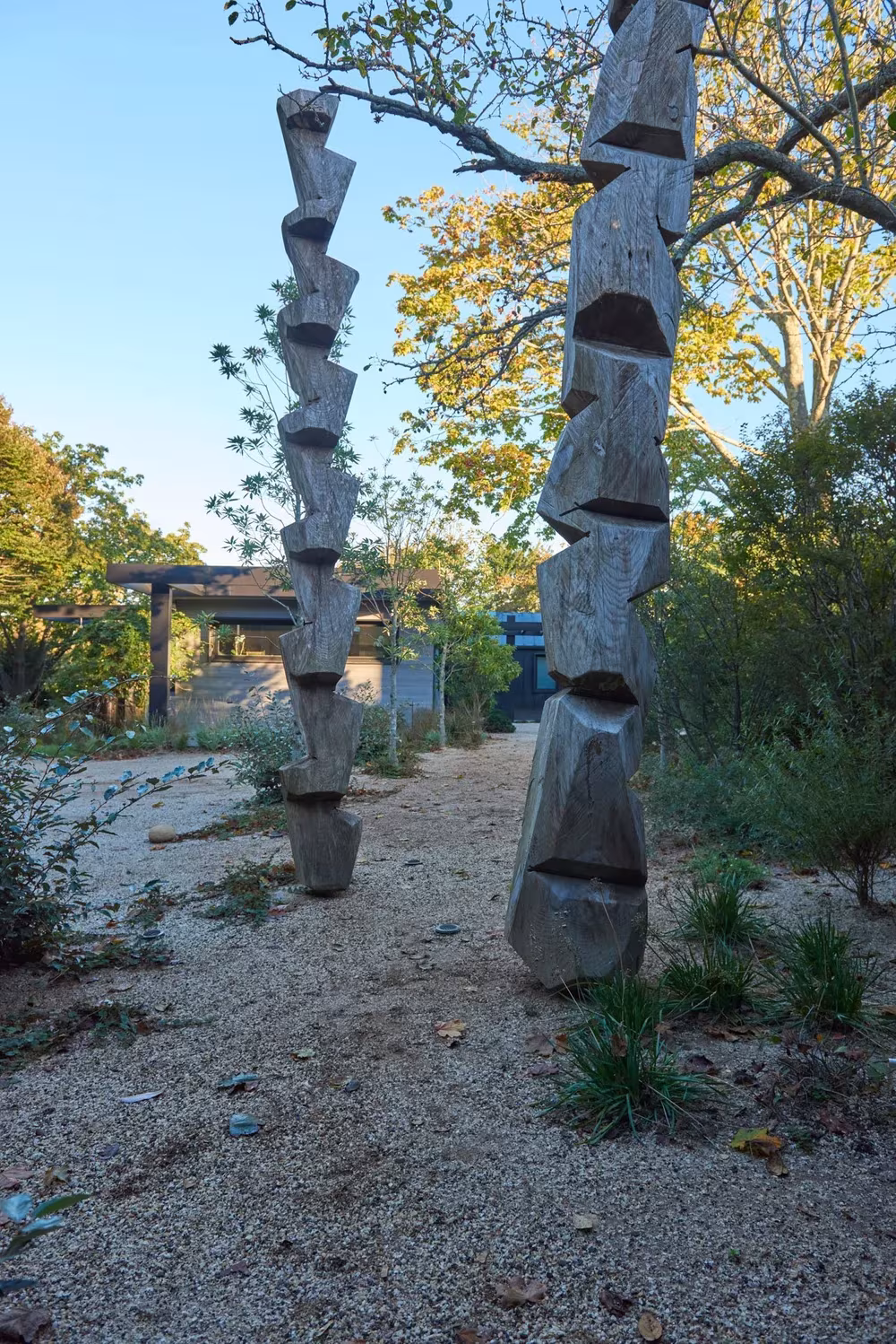 Esculturas verticales de madera tallada en un sendero de grava entre árboles y vegetación nativa