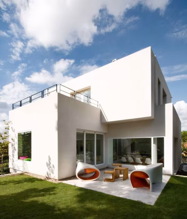 White-volume house with a lawn and orange outdoor armchairs by the glazing