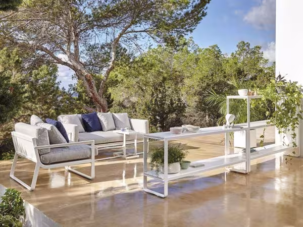 Outdoor sofa set with a white frame, blue cushions and a glass table among pines