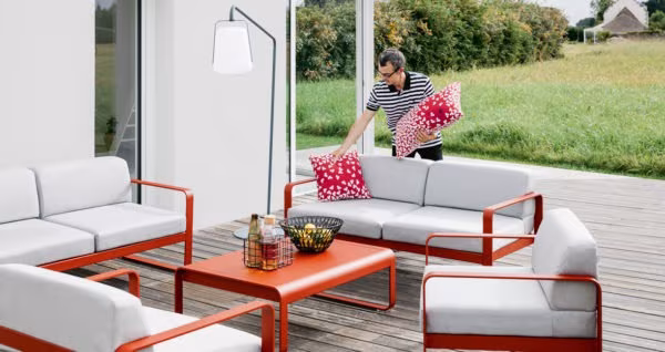 Red metal outdoor sofas and coffee table with grey cushions on decking beside the lawn