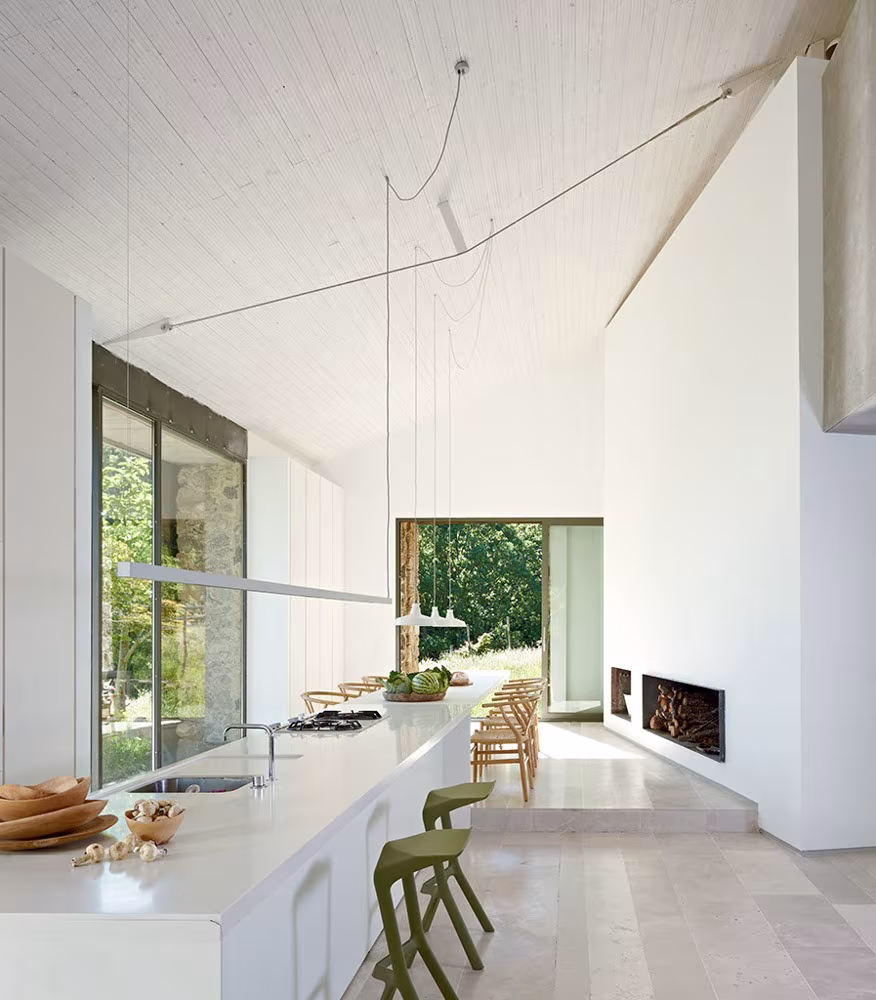 ABATON-finca-en-extremadura-66-2 High-ceilinged kitchen with white island, fireplace and an opening framing the woodland at the Extremadura farmhouse by Ábaton