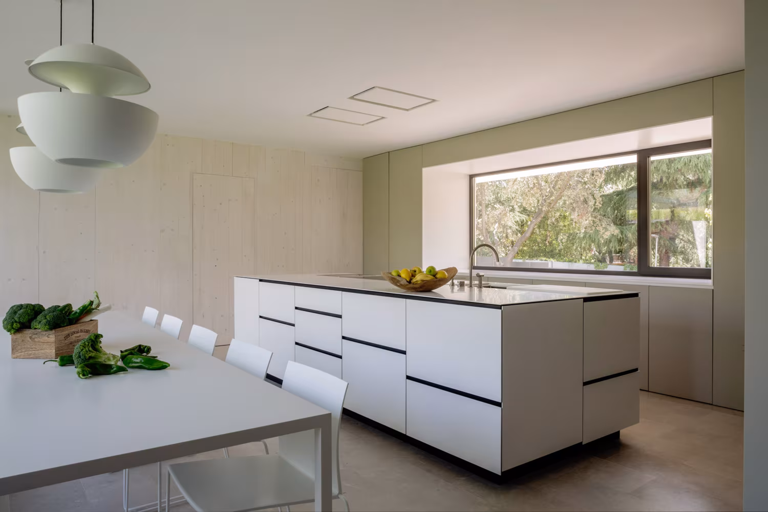 Isla de cocina blanca con cajones de tirador oculto y ventana apaisada sobre el jardín en el Proyecto AF