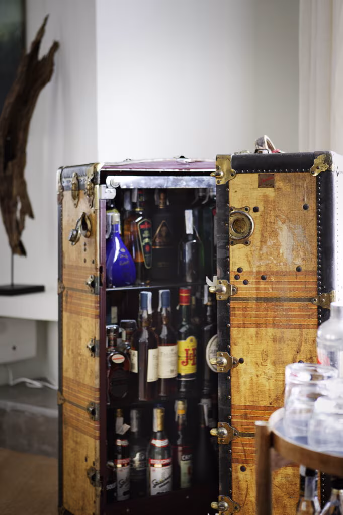 Open travelling trunk bar with bottles beside a sculptural branch in the Rosales refurbishment