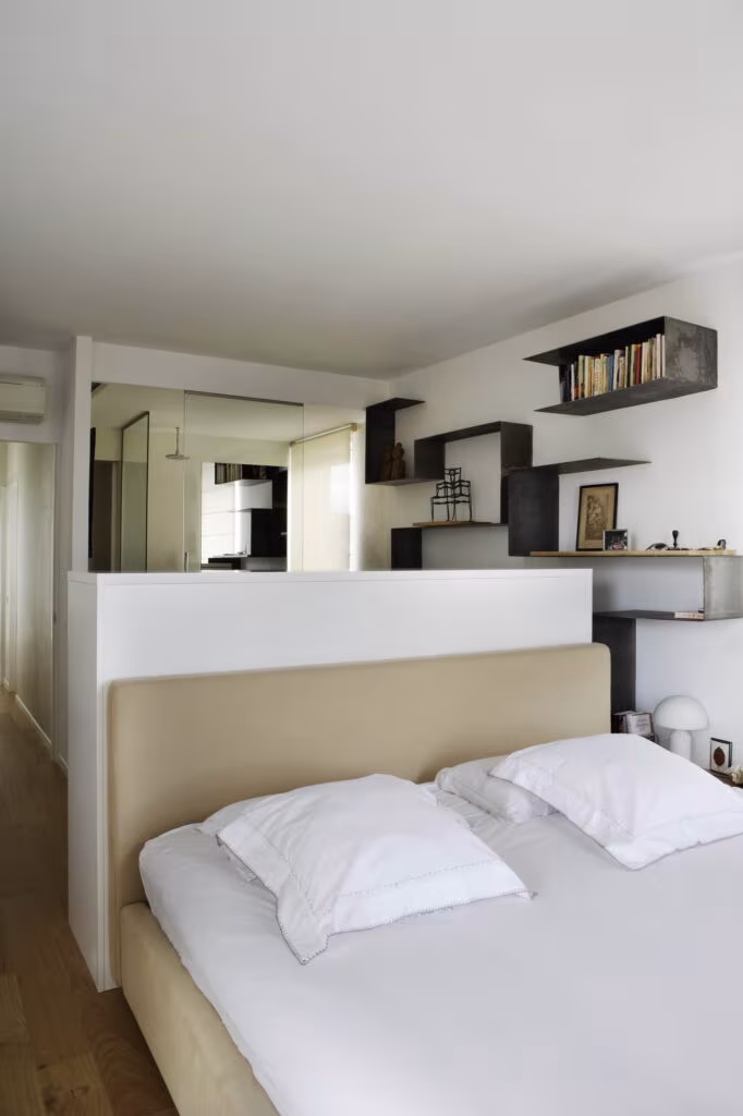 Bedroom with a low headboard dividing it from the bathroom and black iron shelves in the Rosales refurbishment