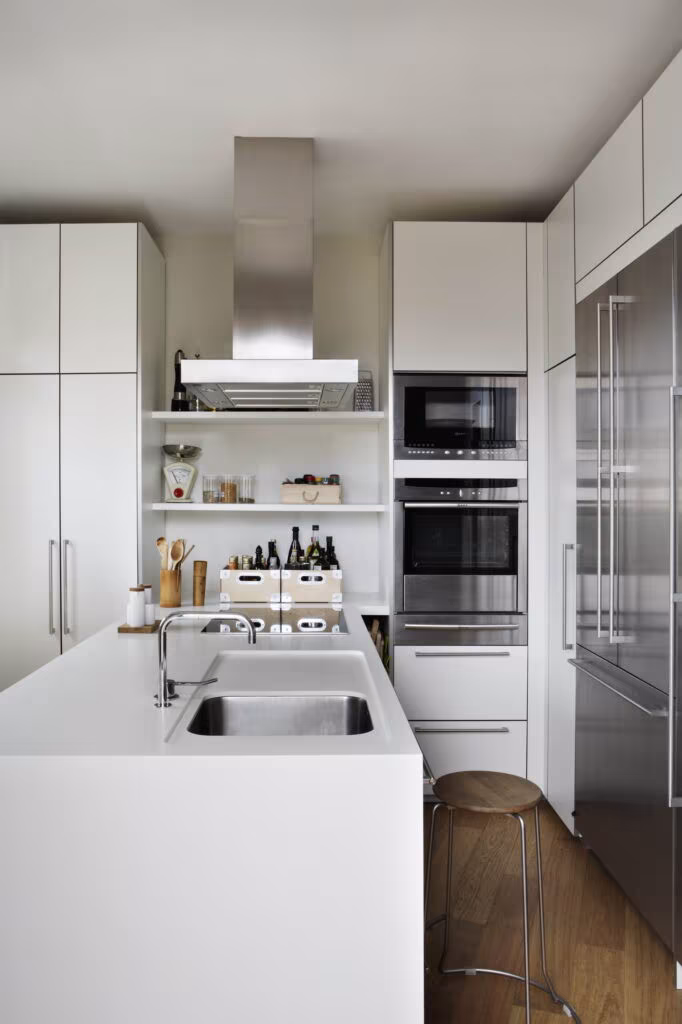 White kitchen with island, sink, oven and steel fridge in the Rosales full refurbishment