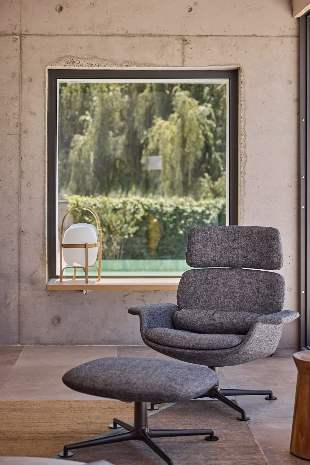 Grey armchair with ottoman before a window in a concrete wall at Casa de las encinas