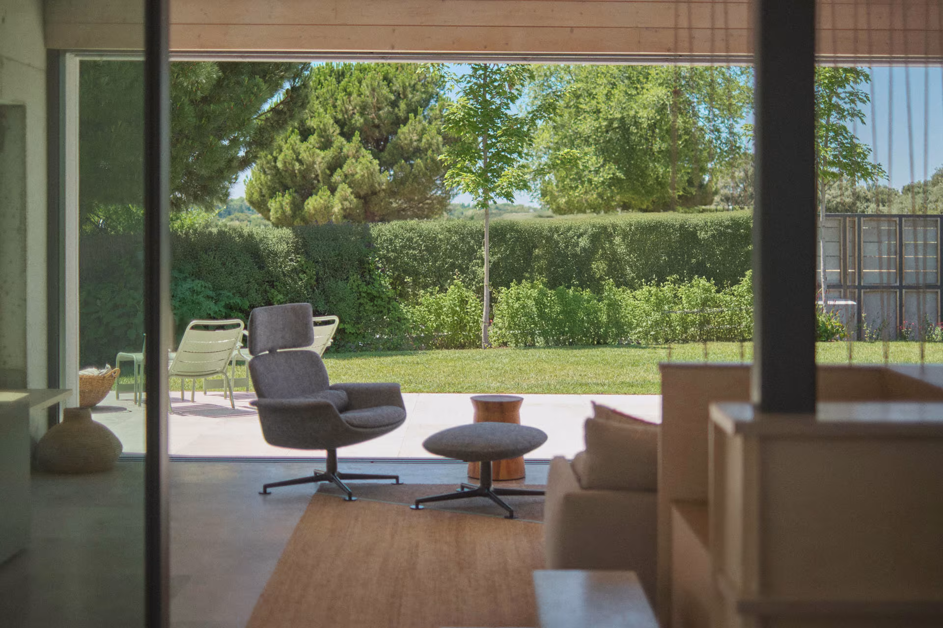 Abaton – Pozuelo 104 Armchair with ottoman in the living room open to the lawn and hedge through the glazing of Casa de las encinas