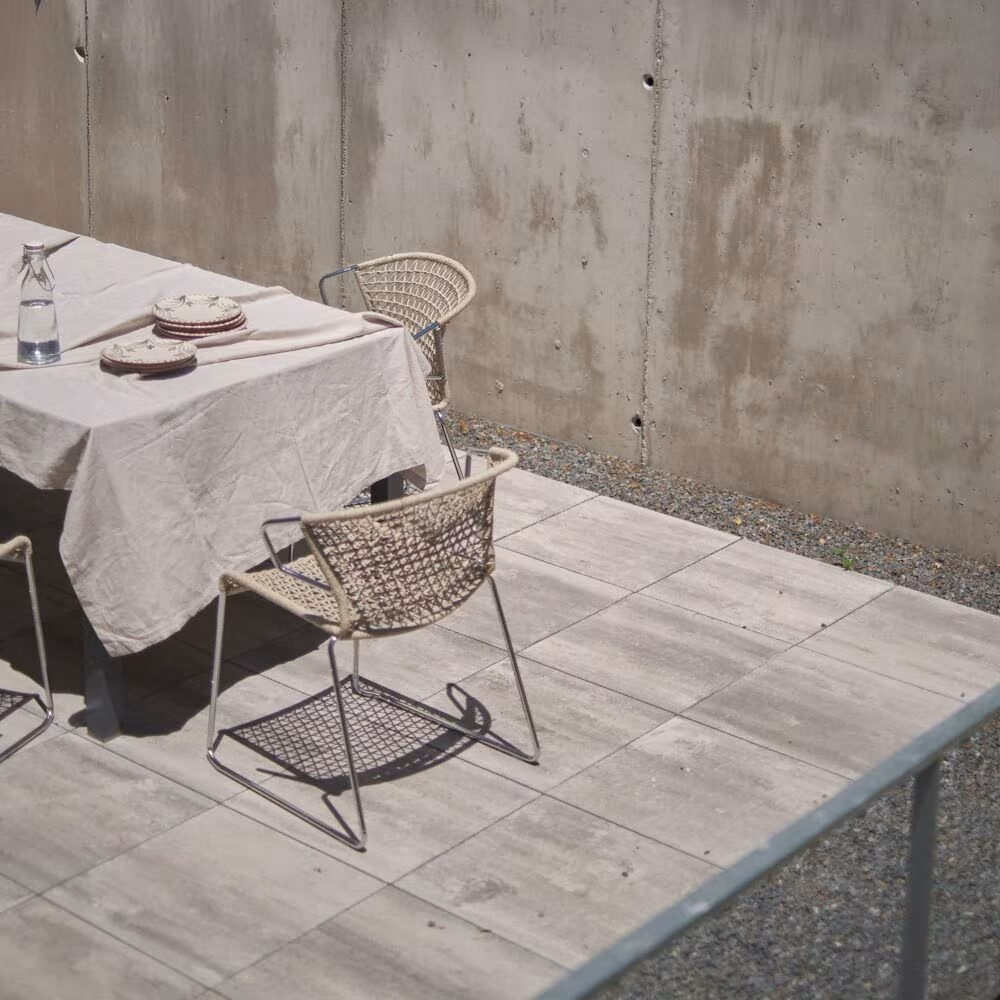 Abaton – Pozuelo 130 Table dressed with a linen cloth and rope chairs on ceramic paving beside a concrete wall in Casa de las encinas