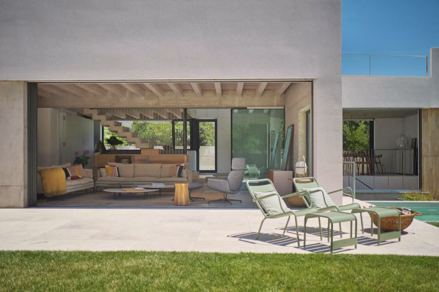 Abaton – Pozuelo 89 Facade of Casa de las encinas open to the garden with porch, green loungers and living room beyond