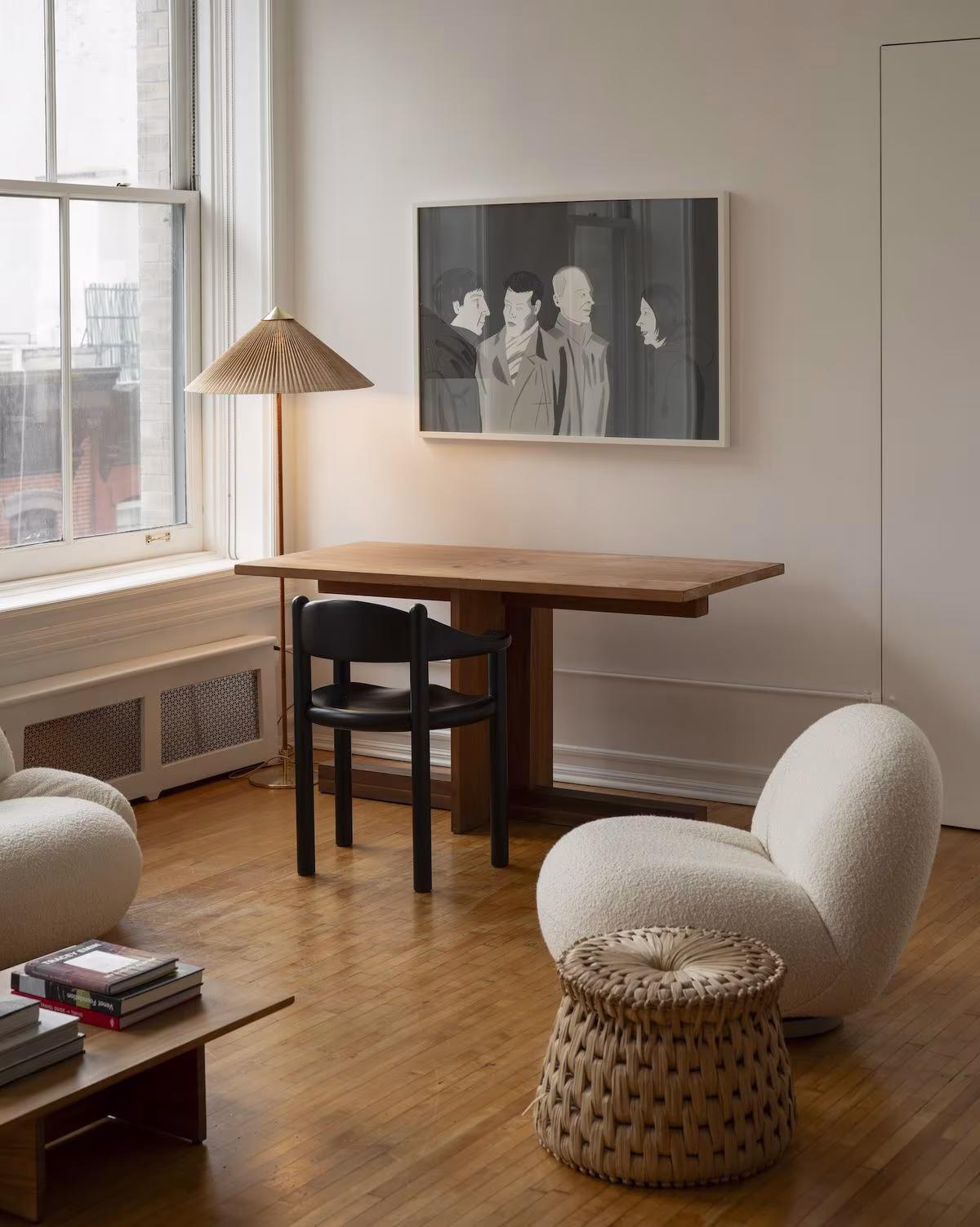Rincón de trabajo con mesa de madera, sillón blanco de bouclé y lámpara de pie junto a una ventana de guillotina