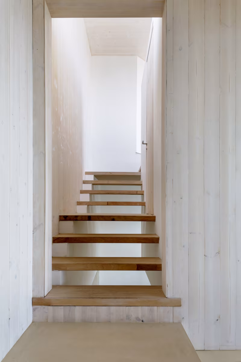 Escalera de peldaños de madera volados entre muros blancos en la reforma Birdhide, en Irlanda