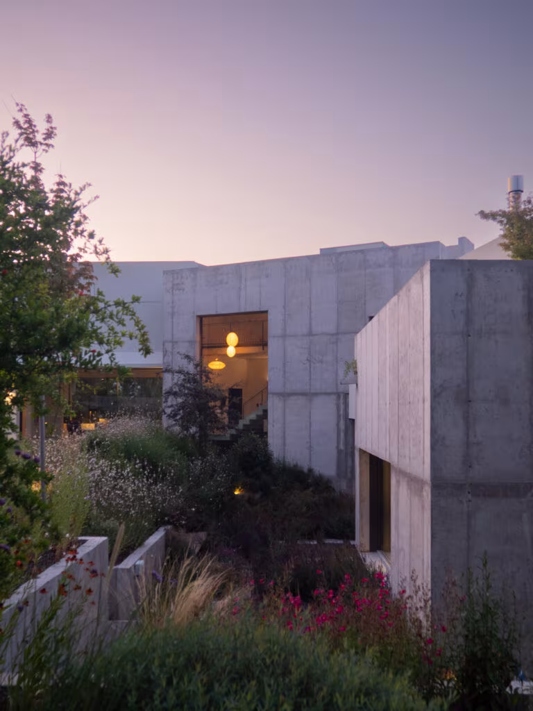 Muros de hormigón con una ventana encendida y jardín de plantación en la Casa ÁRCO de Ábaton al atardecer