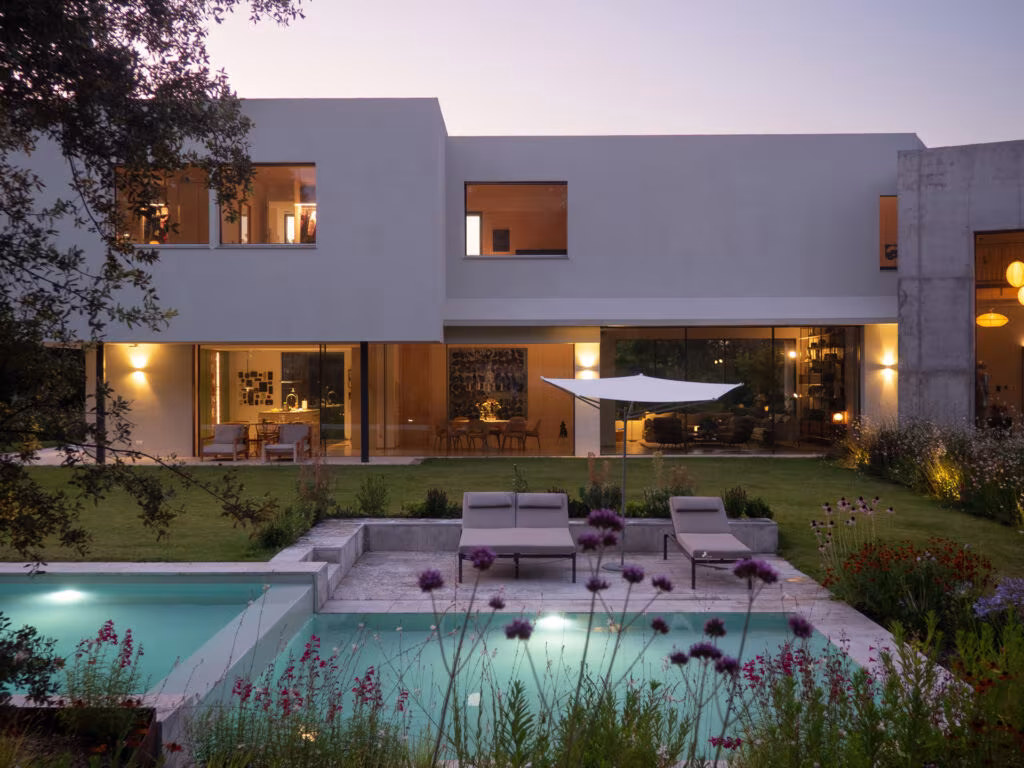 Casa ÁRCO al anochecer con las ventanas iluminadas sobre la piscina escalonada y las tumbonas