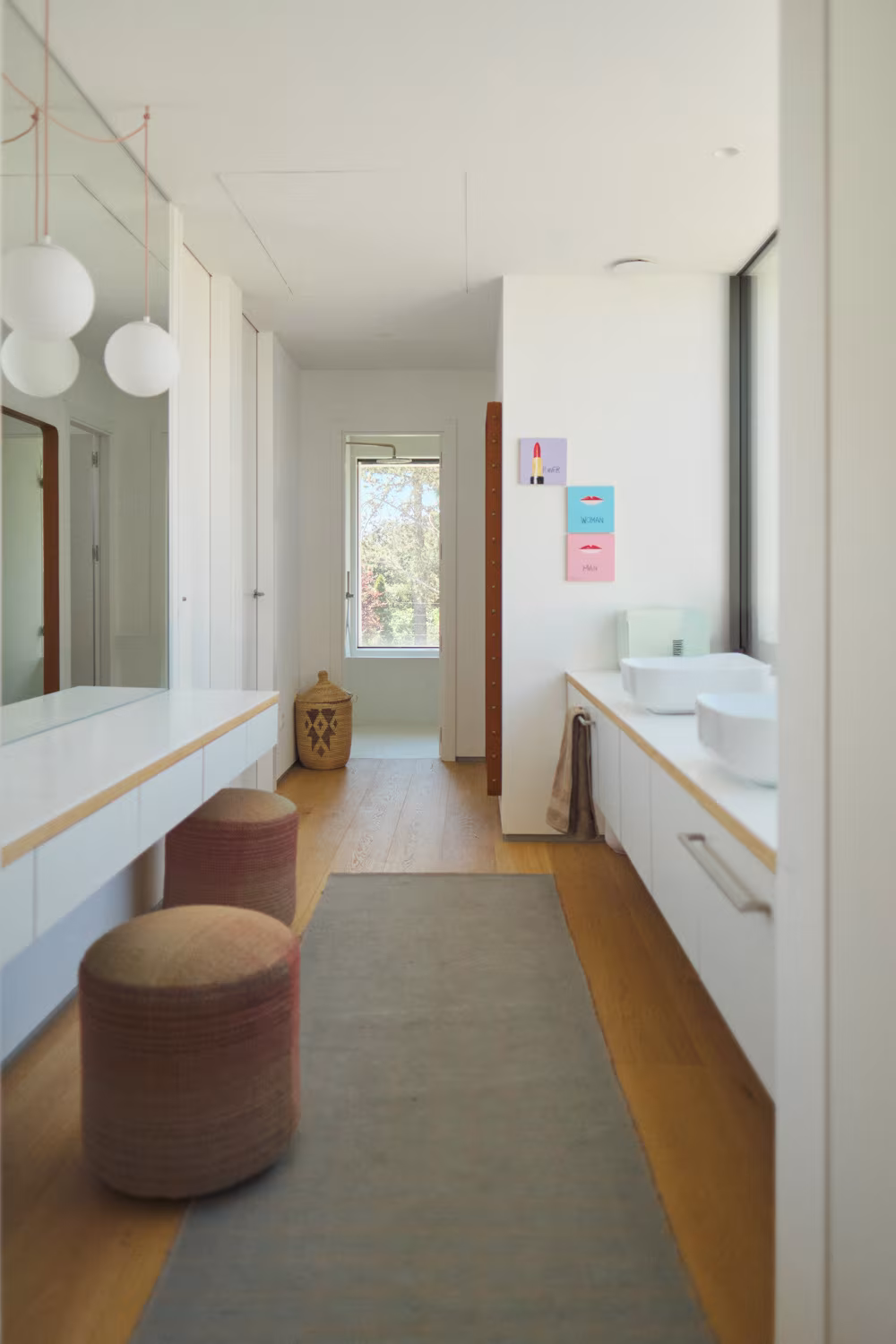 Baño largo con encimera blanca corrida, dos lavabos y pufs de color terracota en la Casa ÁRCO