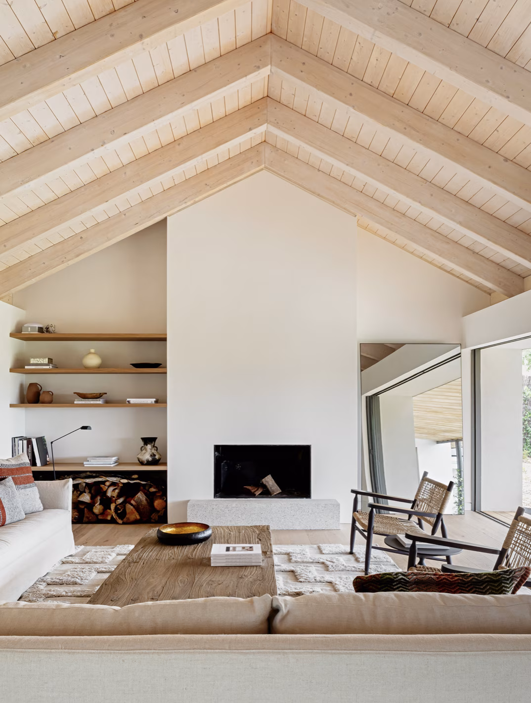Salón bajo techo de vigas de madera a dos aguas, con chimenea blanca y butacas de rejilla en Birdhide