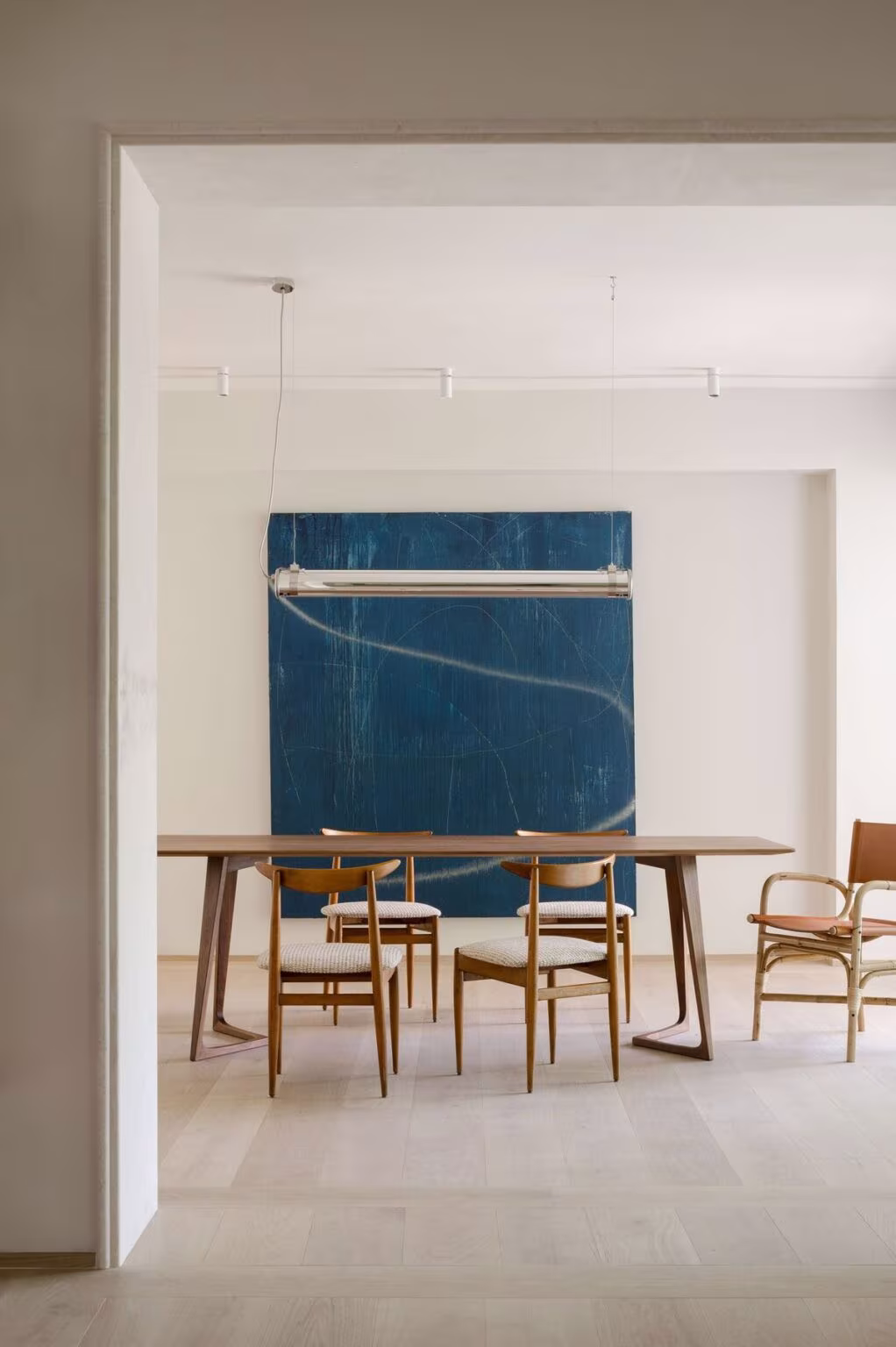 Comedor luminoso con mesa de madera, sillas de rejilla y un gran lienzo azul en Birdhide, Irlanda