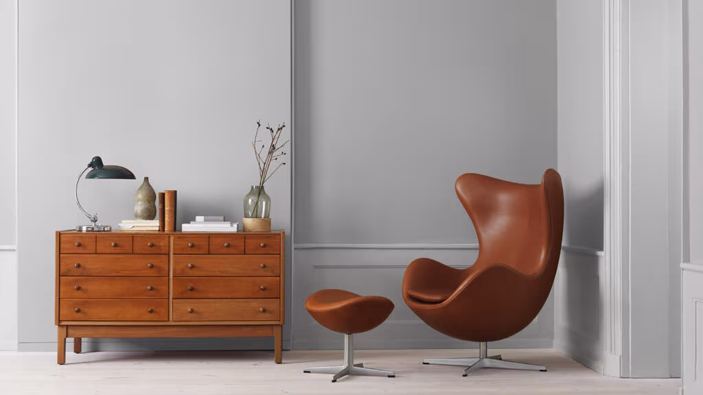 Cómoda de madera de teca y sillón Egg de cuero ante un muro gris, ejemplo del diseño escandinavo