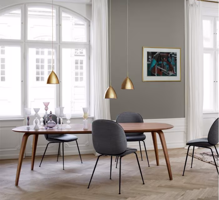 Comedor con mesa ovalada de madera, sillas tapizadas y lámparas de latón en una sala clásica de estilo escandinavo