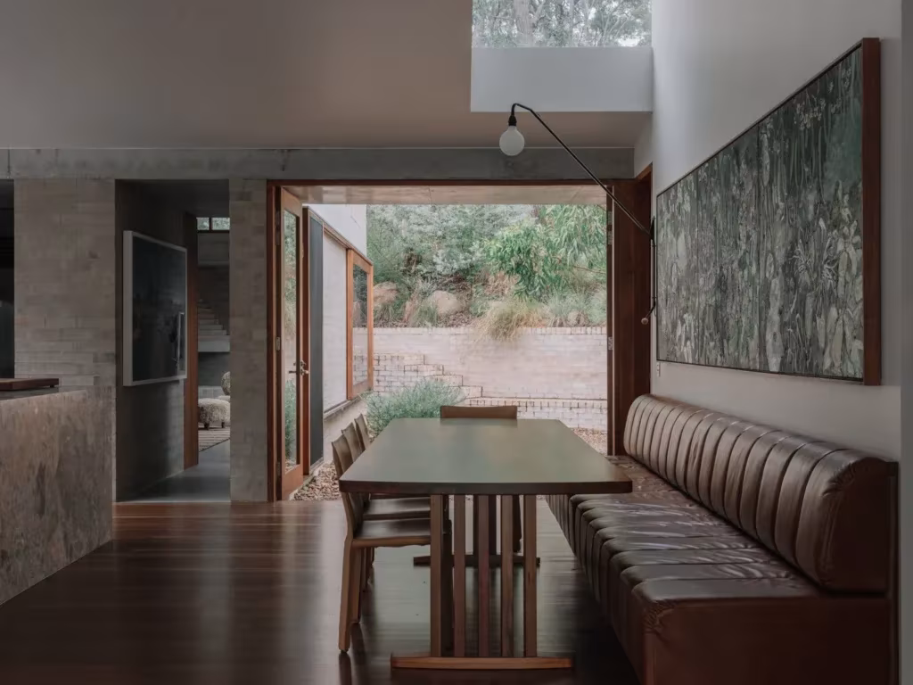 Comedor de la Stuartholme House con banco de cuero, mesa de madera y ventanal al patio