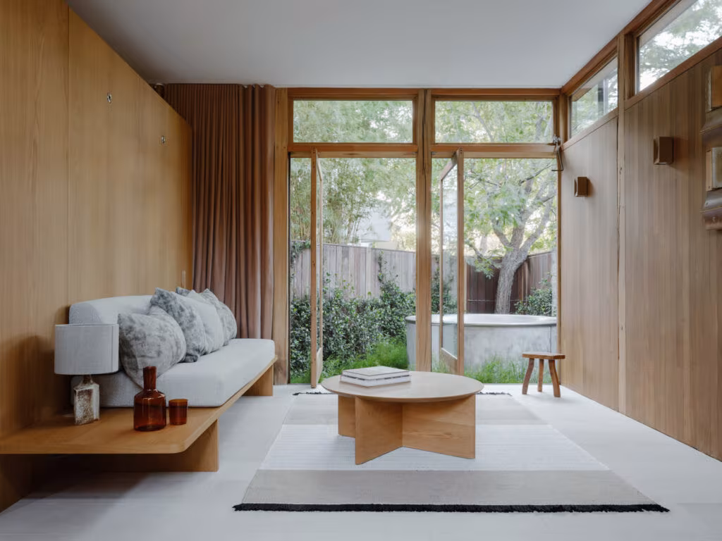 Interior de madera del Love Shack con banco corrido, mesa baja y cristalera al jardín en Sídney