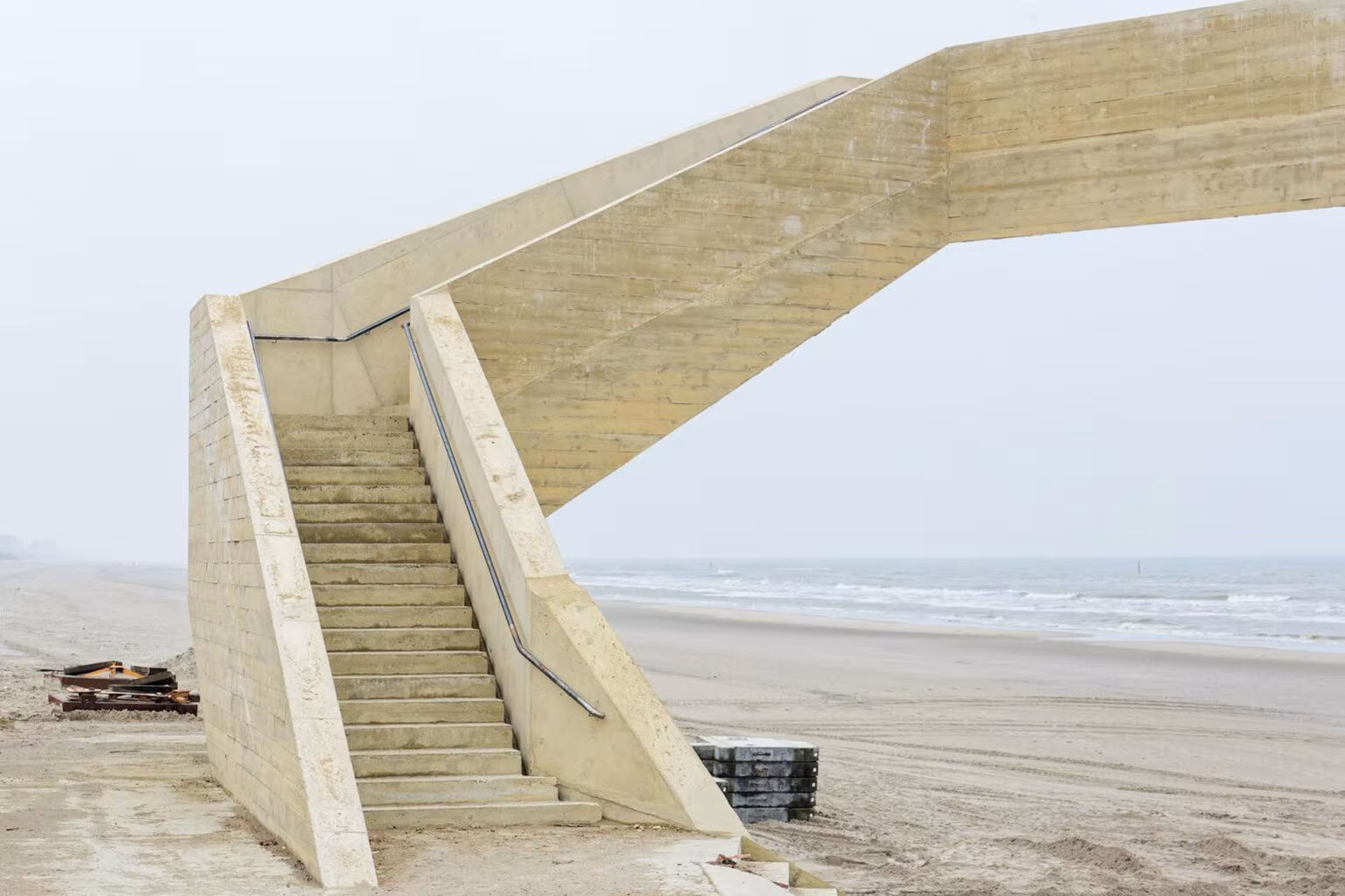 Rampa y escalera de hormigón de Westerpunt elevadas sobre la playa en un día nublado