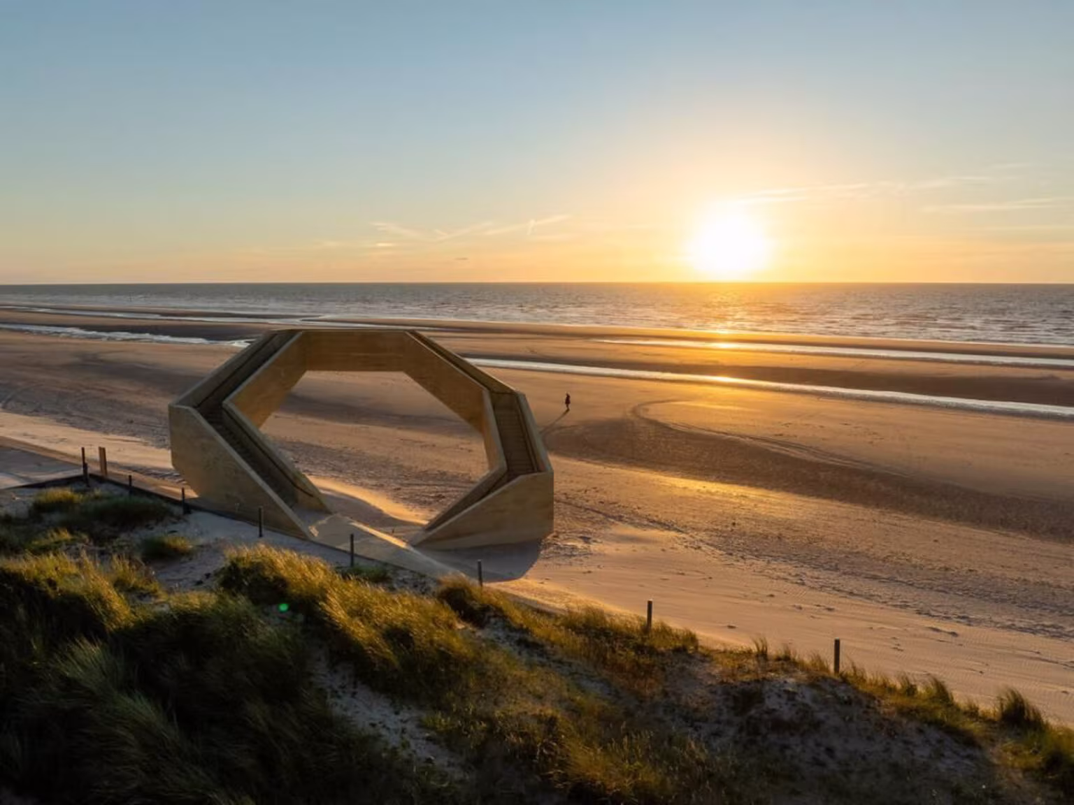 Westerpunt recortado contra el sol poniente sobre la playa con dunas en primer plano
