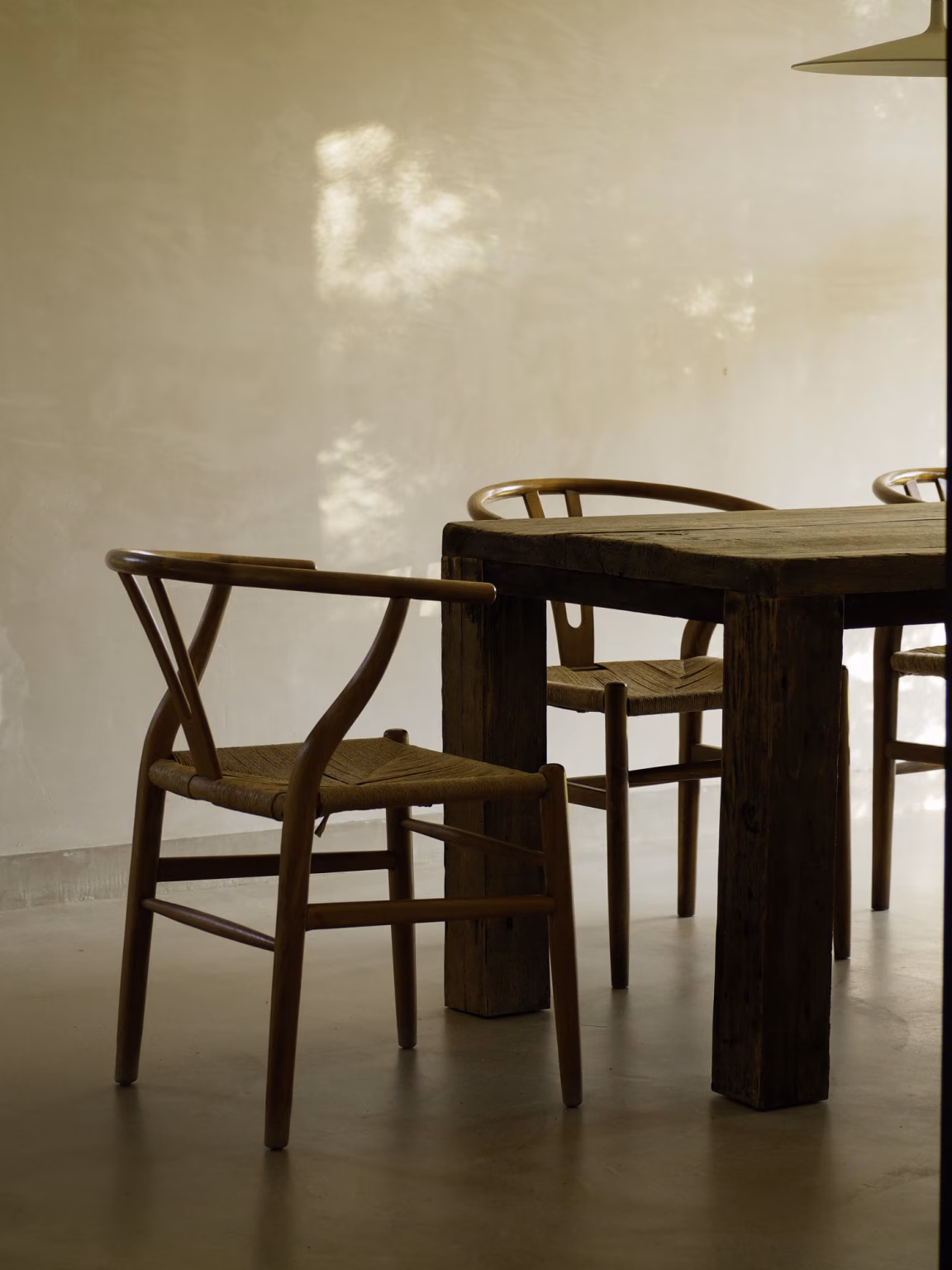 Detalle de mesa de madera envejecida y sillas de madera con asiento de cuerda en Villa Arena