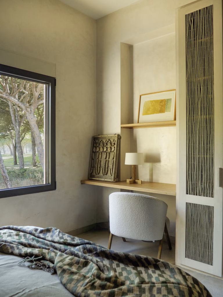 Dormitorio con escritorio empotrado, silla blanca y ventana al pinar junto a un armario de lamas en Villa Arena