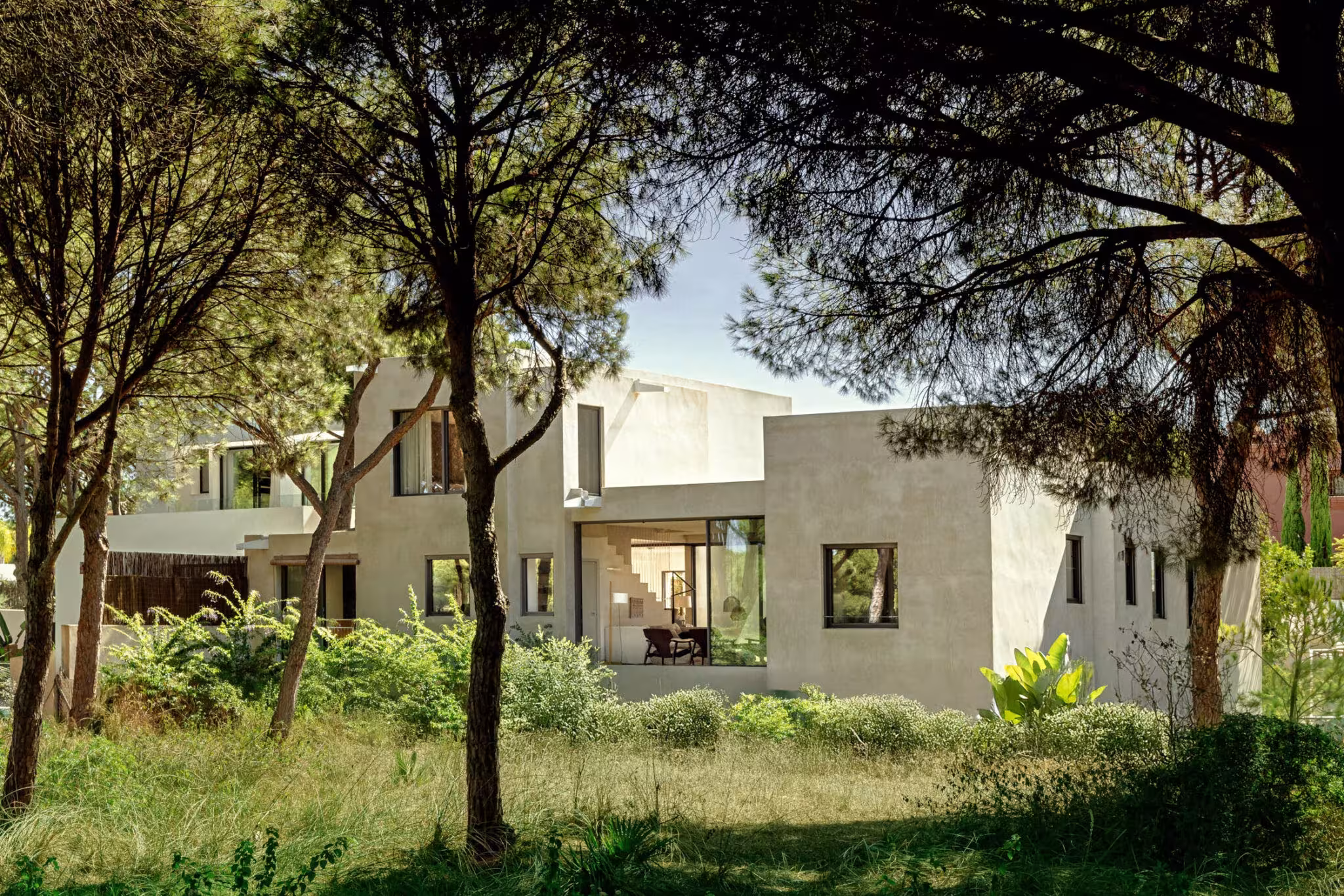 Volúmenes de microcemento de Villa Arena entre pinos y hierba vistos desde la parcela