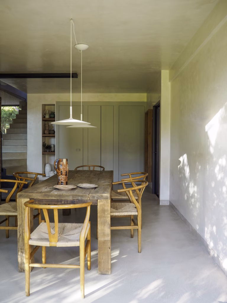 Comedor de Villa Arena en profundidad, con mesa larga de madera, sillas amarillas y escalera al fondo