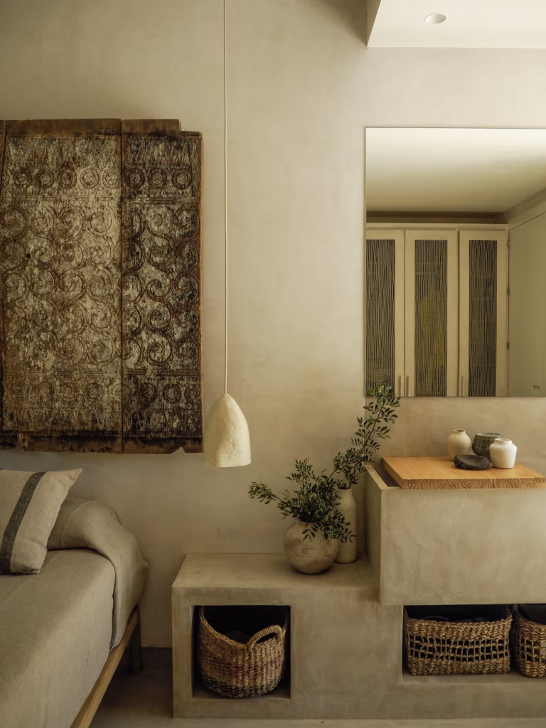 Rincón de dormitorio con armario antiguo tallado, banco de obra y cesta de mimbre en Villa Arena