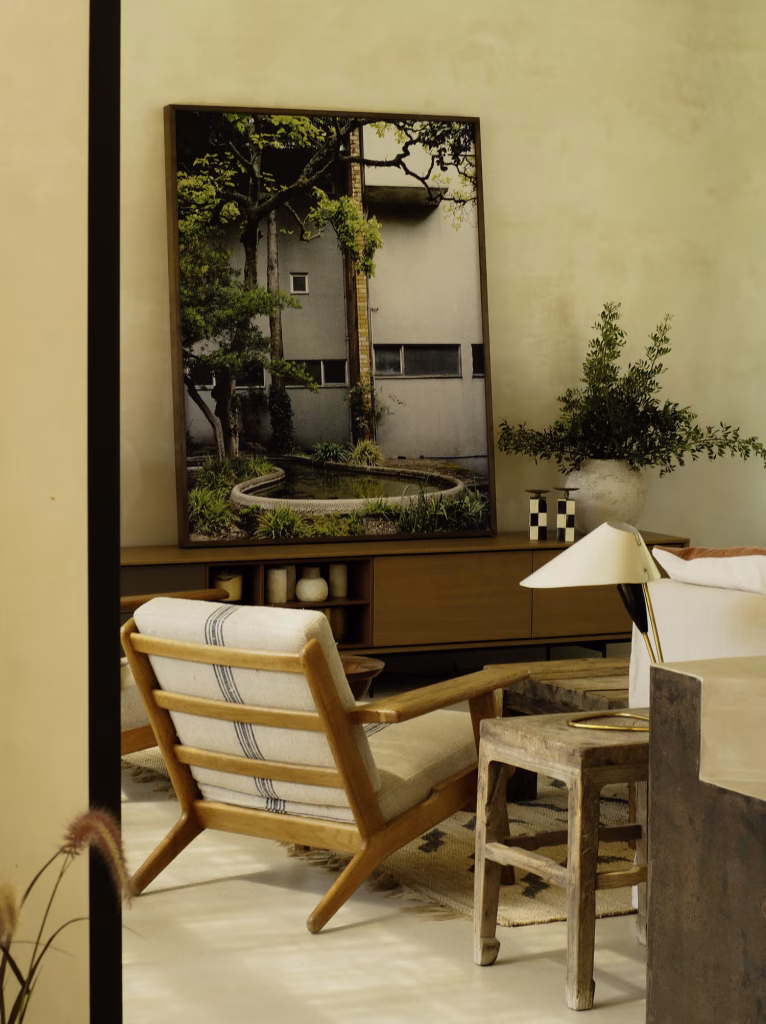 Butaca de madera y mueble bajo un gran espejo que refleja un patio con vegetación en Villa Arena