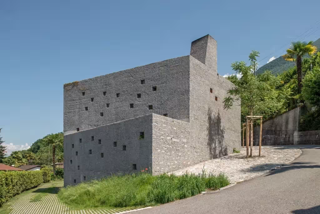 Volumen de piedra con huecos cuadrados y chimenea junto a la calle en San Nazzaro de Wespi de Meuron Romeo