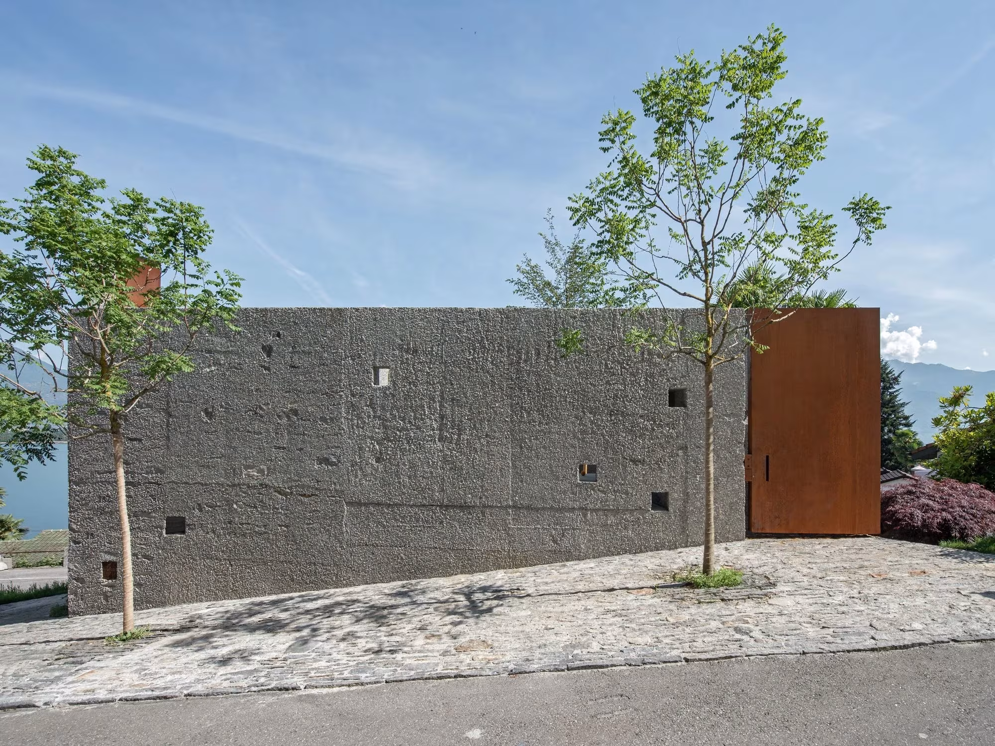 Muro de piedra con puerta de acero corten y árboles en el frente de la casa San Nazzaro, Wespi de Meuron Romeo