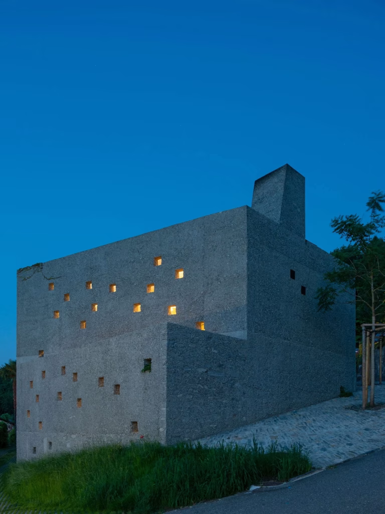 Casa San Nazzaro al anochecer con los huecos iluminados sobre el muro de piedra y la chimenea al fondo