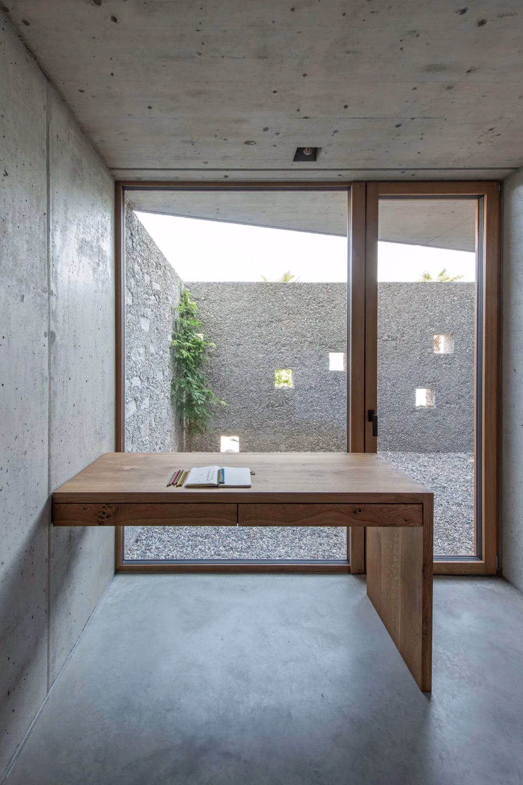 Escritorio de madera junto a un patio de piedra visto a través de un ventanal en la casa San Nazzaro