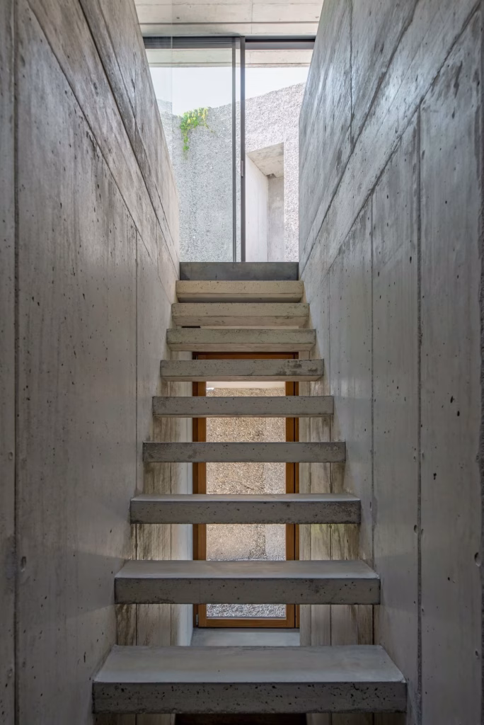 Escalera de peldaños de hormigón entre muros de hormigón visto que baja hacia un patio en la casa San Nazzaro