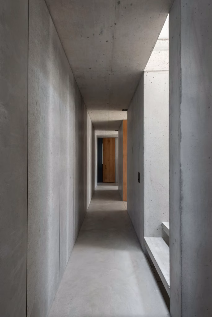 Pasillo de hormigón visto con banco corrido y luz natural al fondo en la casa San Nazzaro
