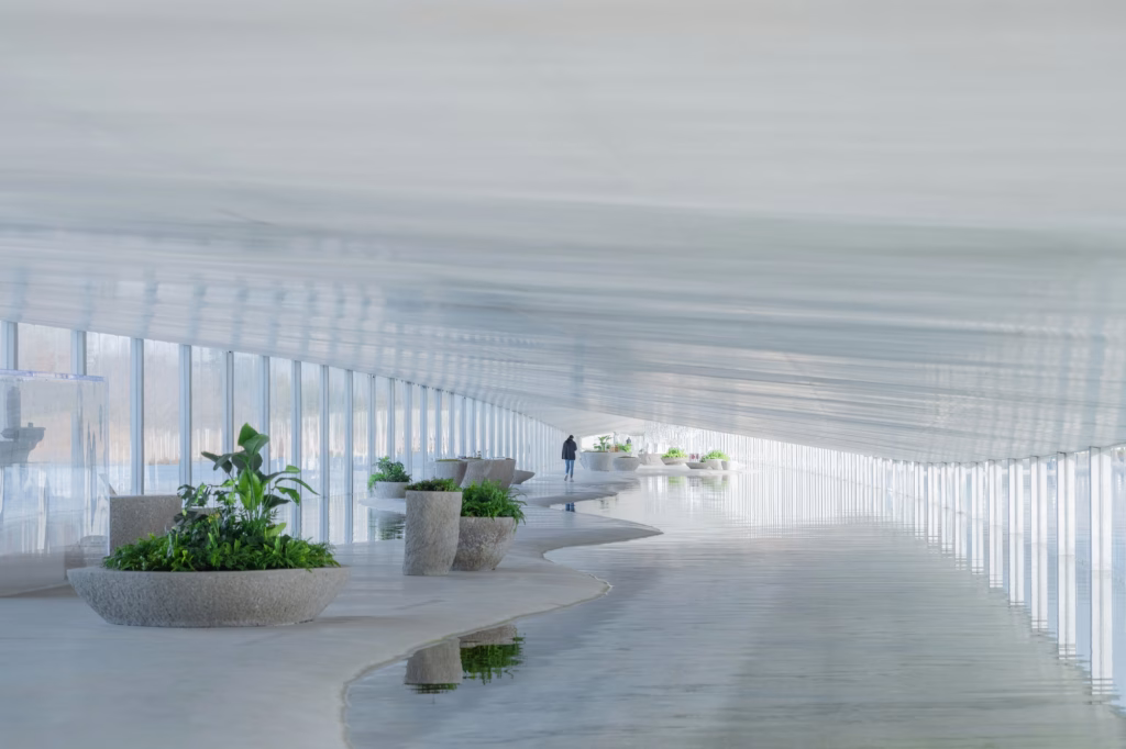 Interior diáfano del museo Zaishui con suelo ondulado, plantas y estanques bajo el techo blanco, de Junya Ishigami