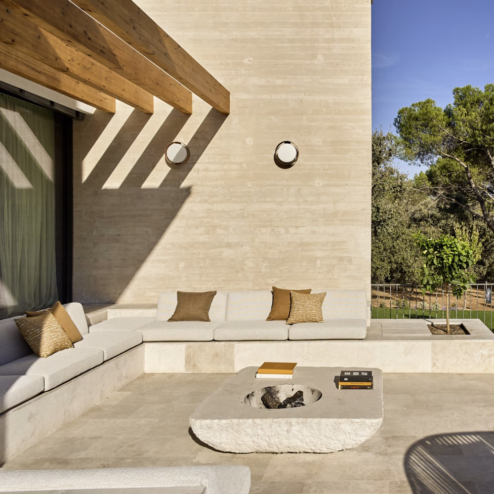 Sunken outdoor lounge with L-shaped sofa, stone table and timber pergola by the concrete wall, Escorzonera