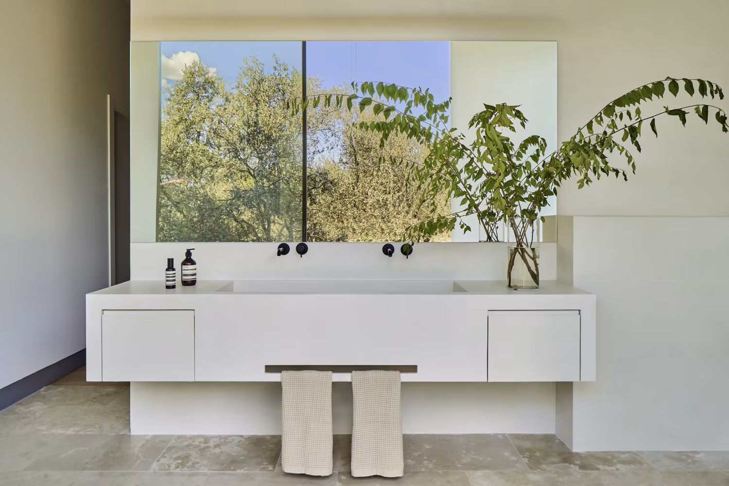 White continuous vanity with black taps and a mirror reflecting the trees in a Escorzonera bathroom