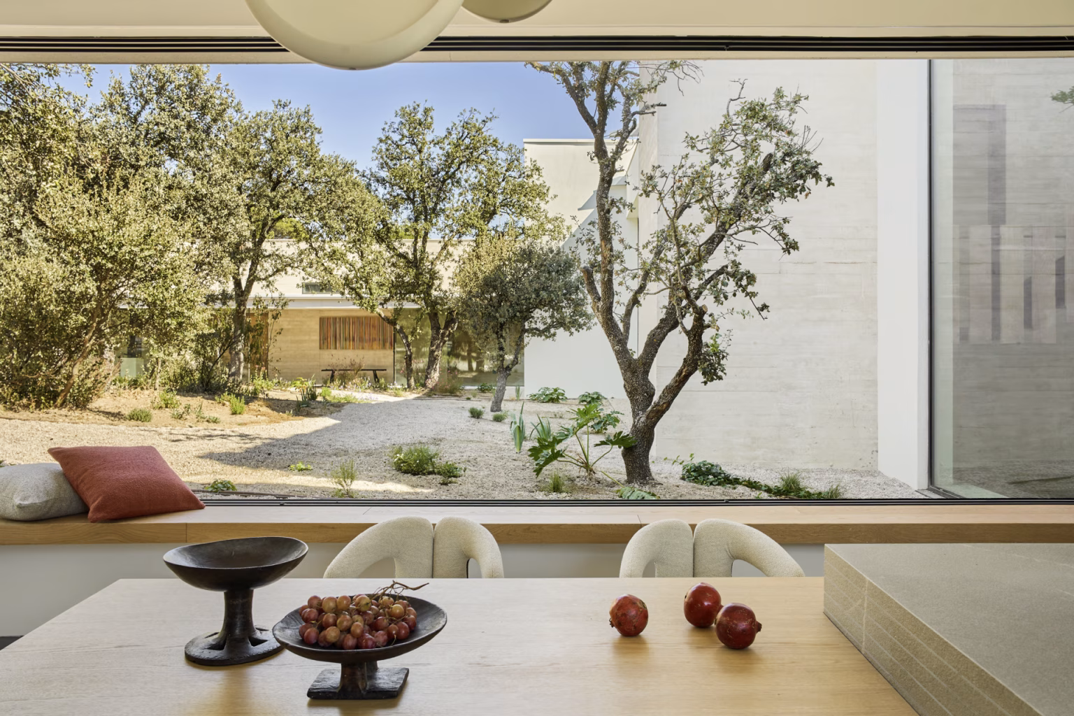 Dining table facing a wide window that frames a holm oak and the gravel courtyard, Escorzonera