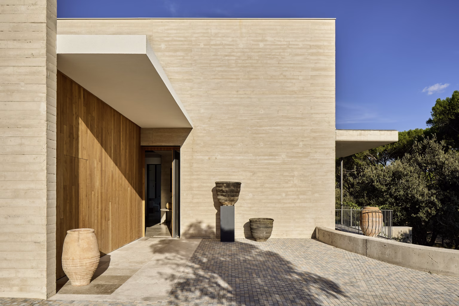 Entrance of the Escorzonera under a canopy, with a timber door and board-formed concrete wall, Proyecto EN