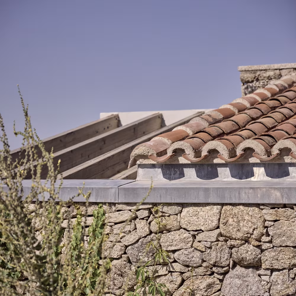 Cubierta de teja árabe y muro de mampostería con nervios de hormigón blanco en el Proyecto TLV