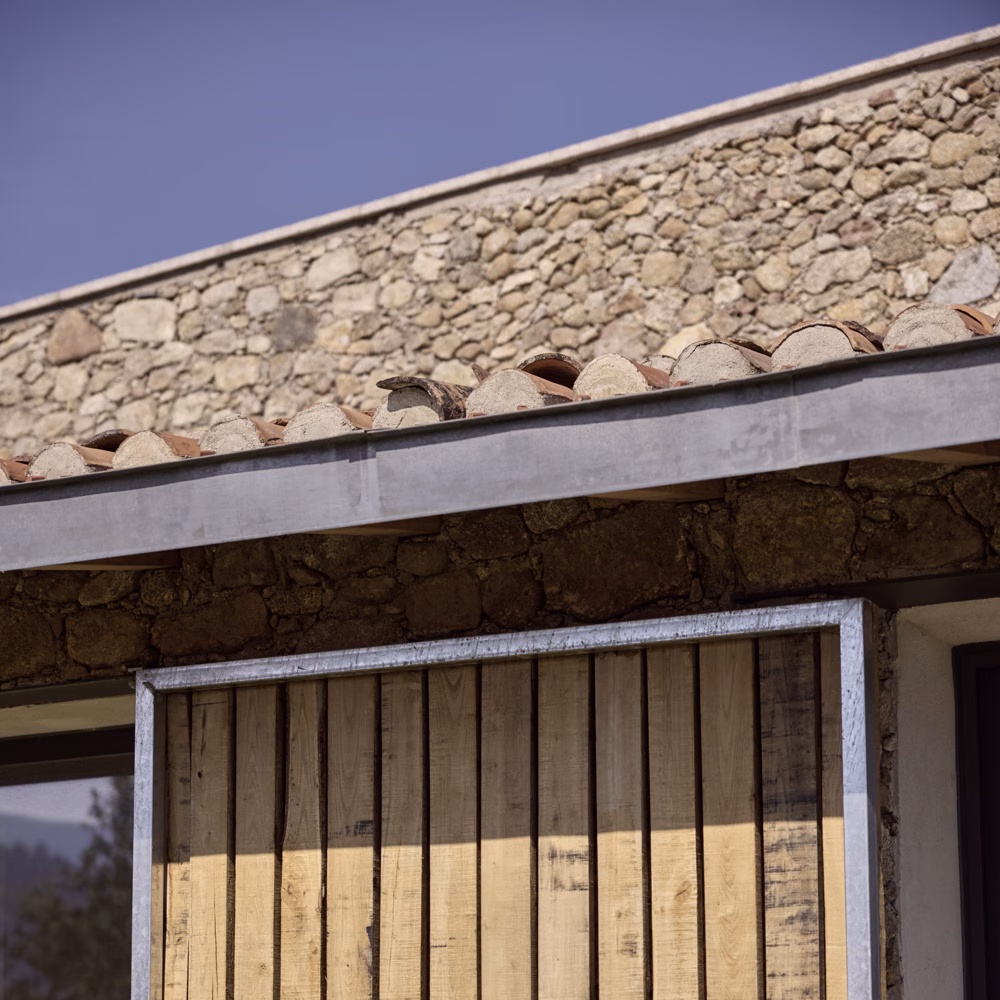 Detalle del alero de teja y de una contraventana de listones de madera con marco metálico en la casa TLV
