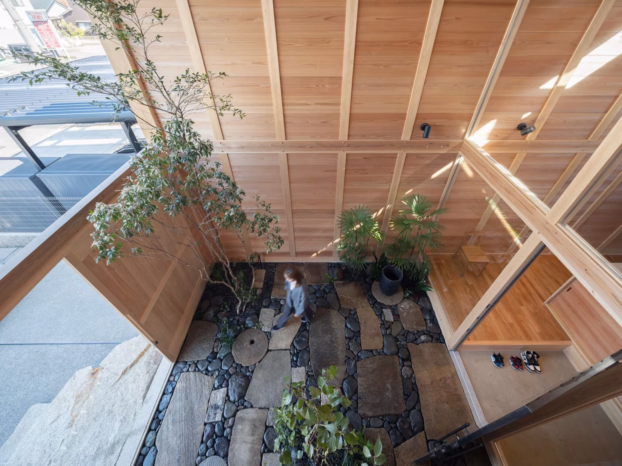 Patio interior con piedras, plantas y luz cenital bajo el entramado de cedro de la casa en Aichi