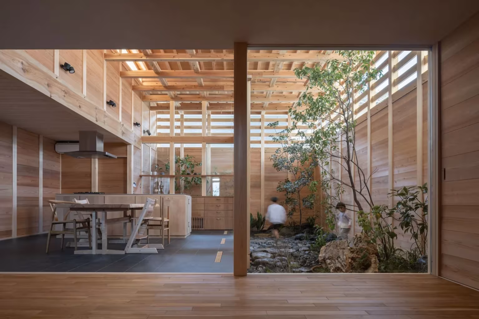 Estancia de la casa en Aichi con mesa de madera junto al patio de piedras y plantas tras un gran cristal
