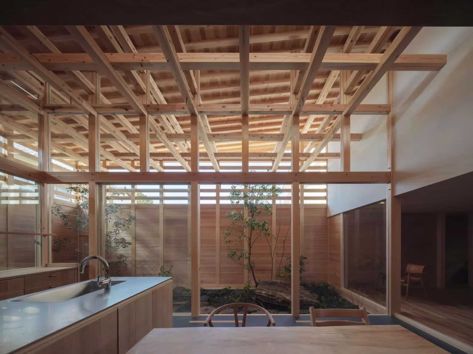 Cocina de acero y madera bajo el entramado de vigas de cedro con patio al fondo en la casa en Aichi