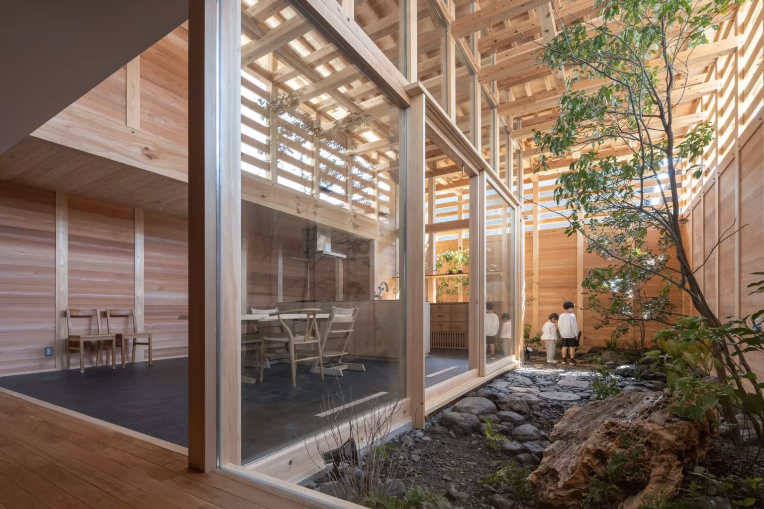Vista del patio con árbol y roca desde la sala, con pilar de madera y lamas de cedro filtrando la luz en Aichi