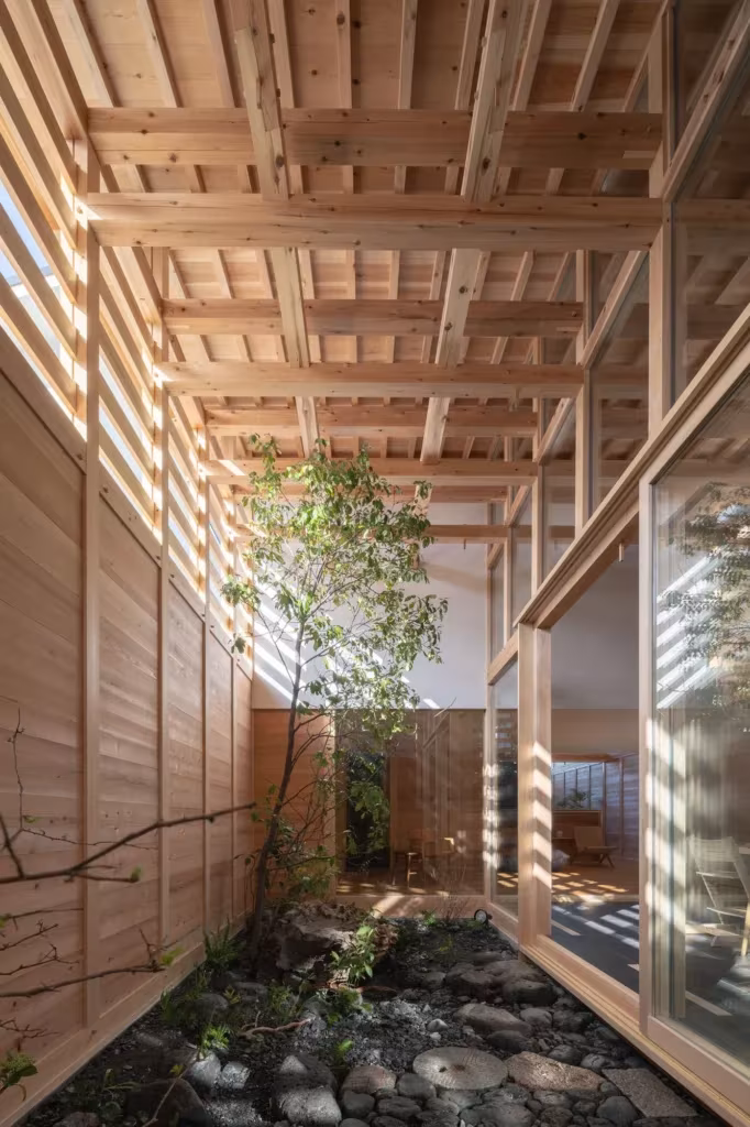 Corredor estrecho de la casa en Aichi con patio de cantos rodados y celosía de cedro que deja pasar la luz cenital